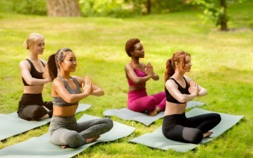 Yoga for peace of mind. Diverse young women sitting in lotus pose and meditating at green park