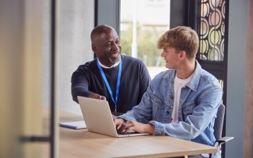 Male University Or College Student With Laptop Having Individual Meeting With Tutor